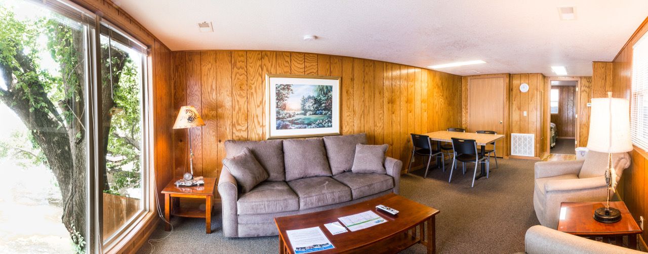 A cozy room with a wooden paneled wall, a sofa, a coffee table, and a dining area with chairs.