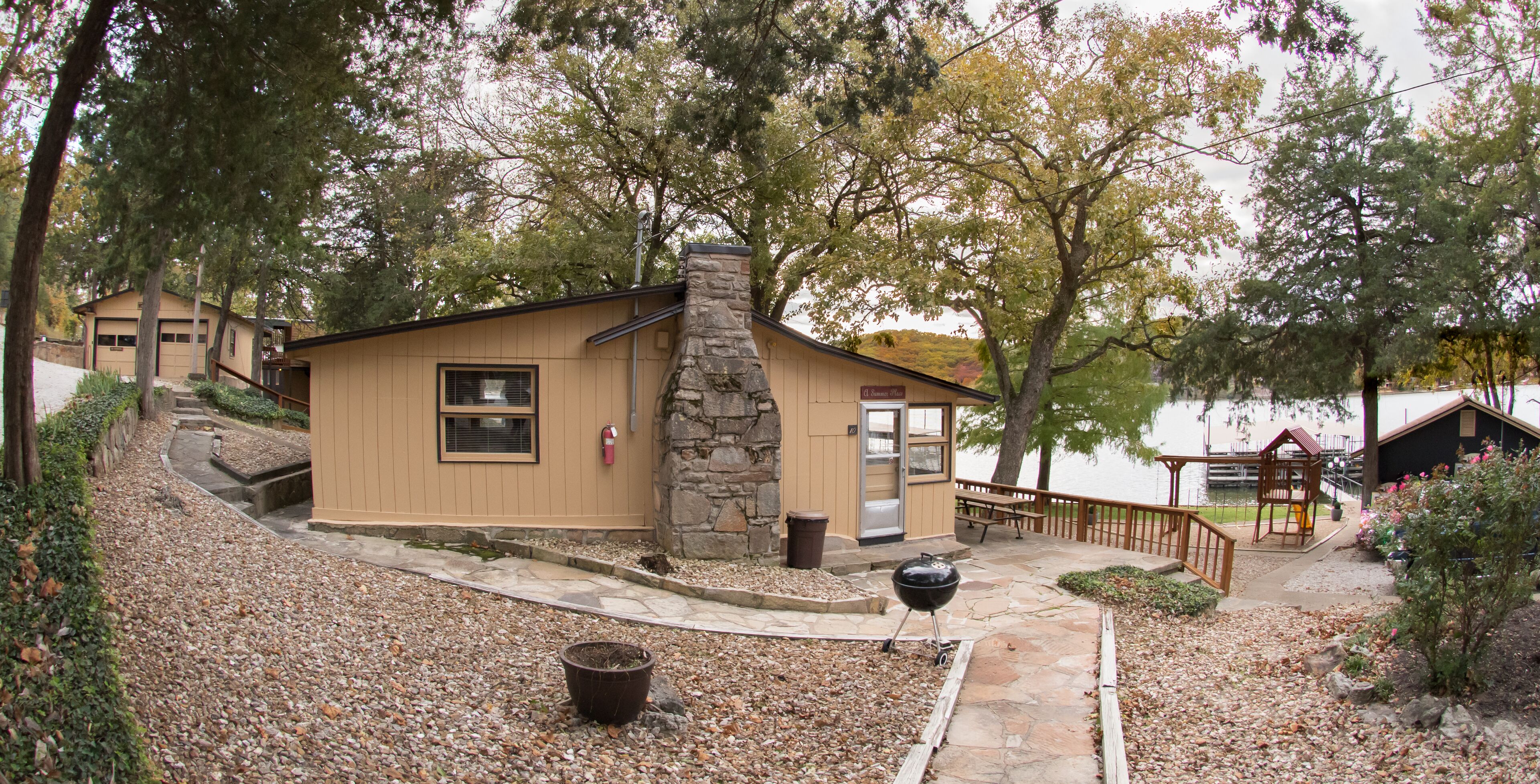 Un pequeño refugio con chimenea de piedra, un patio con parrilla y vistas a un lago.