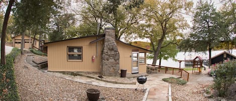 Un pequeño refugio con chimenea de piedra, un patio con parrilla y vistas a un lago.