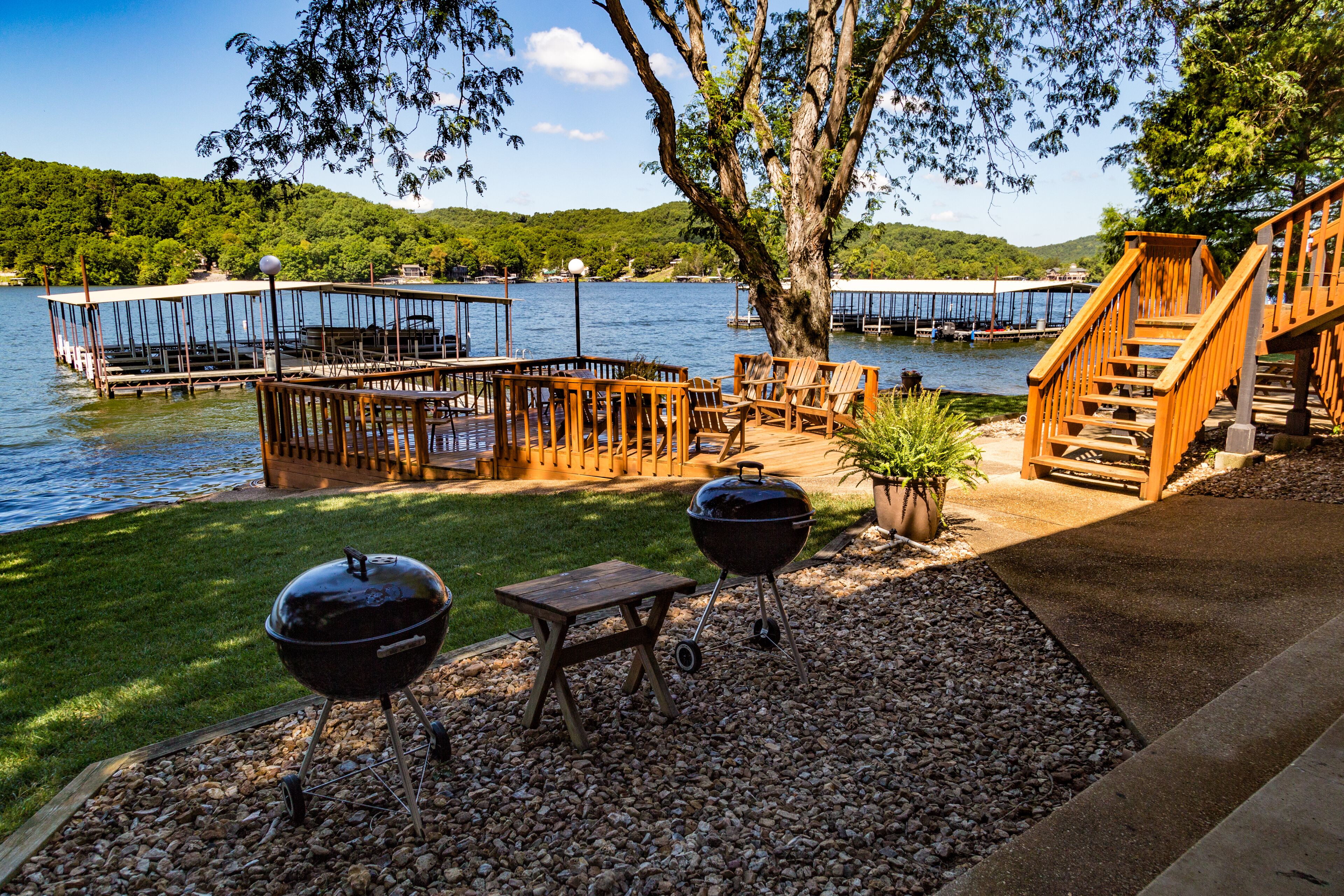 Une terrasse au bord du lac, aménagée avec du mobilier d’extérieur, un barbecue et un escalier menant à un quai.
