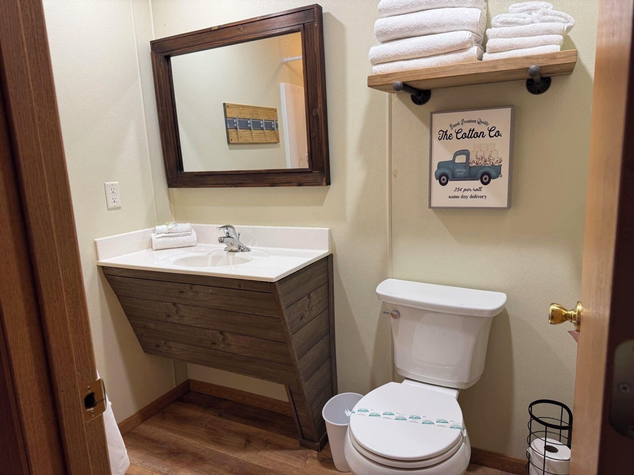 A bathroom with a wooden vanity, a white sink, a mirror, a toilet, and a shelf with towels.