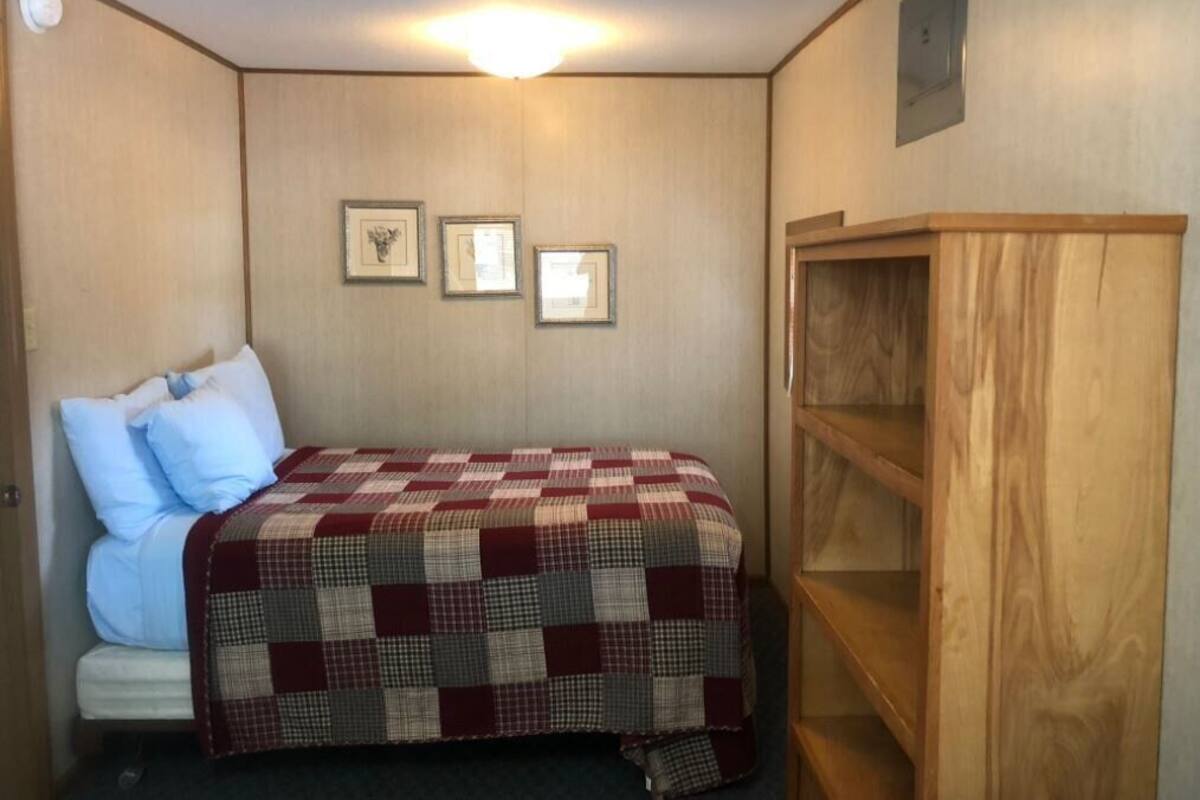A small, cozy room with a single bed, a wooden wardrobe, and three framed pictures on the wall.