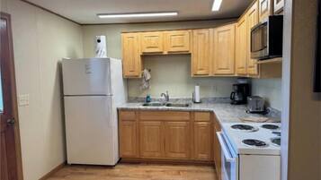 A compact kitchen with wooden cabinets, a refrigerator, a microwave, a stove, and a sink.