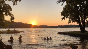 En solnedgång över en sjö, med människor som badar och leker på stranden.