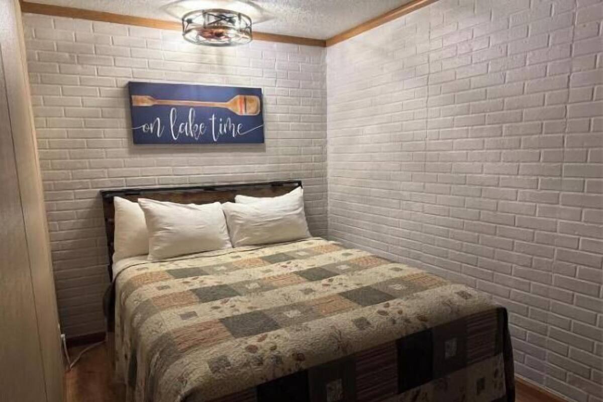A bedroom with a brick-patterned wall, a bed with a quilt, and a sign above the bed that reads "on lake time".