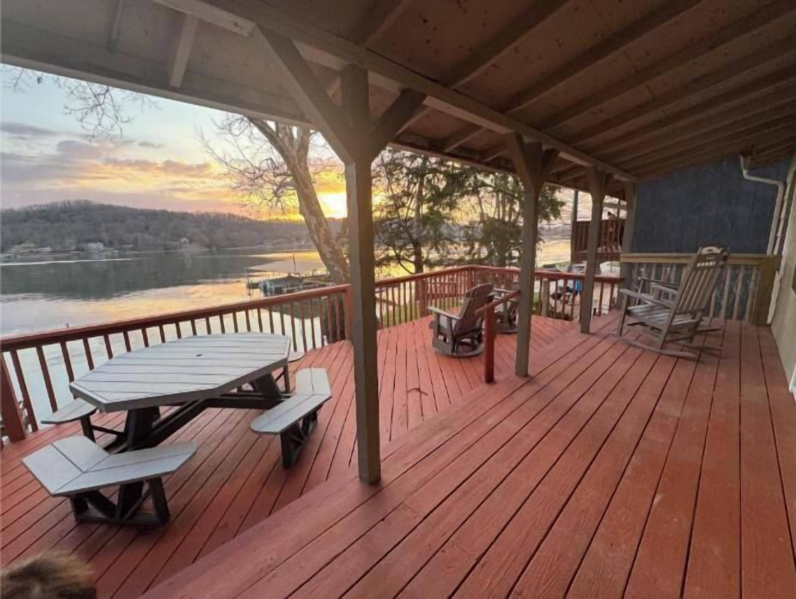 A wooden deck with picnic tables and chairs, overlooking a body of water and hills.