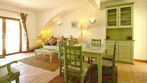 A cozy living room with a dining table, green chairs, a sofa with cushions, a lamp, and a kitchen area with cabinets. - Giddah Green Apartment, Pool, Wifi, AC (Olhos de Água)