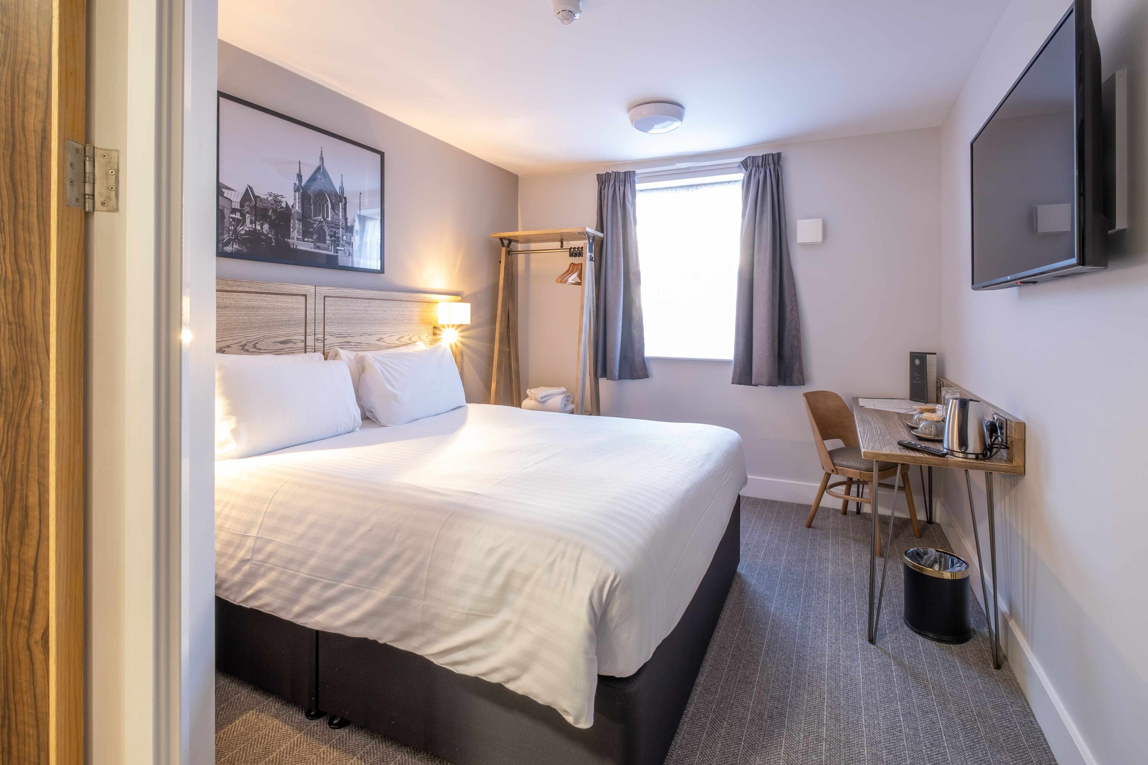 A hotel room with a bed, a desk, a chair, a television, and a window with curtains.