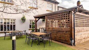 Un patio con una mesa y sillas de madera, una valla de madera y un edificio al fondo.