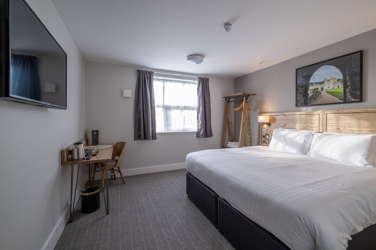 A hotel room with a large bed, a desk with a chair, a TV, and a window with curtains.