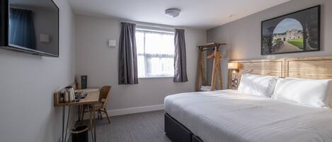 Een hotelkamer met een groot bed, een bureau met stoel, een televisie en een raam met gordijnen.