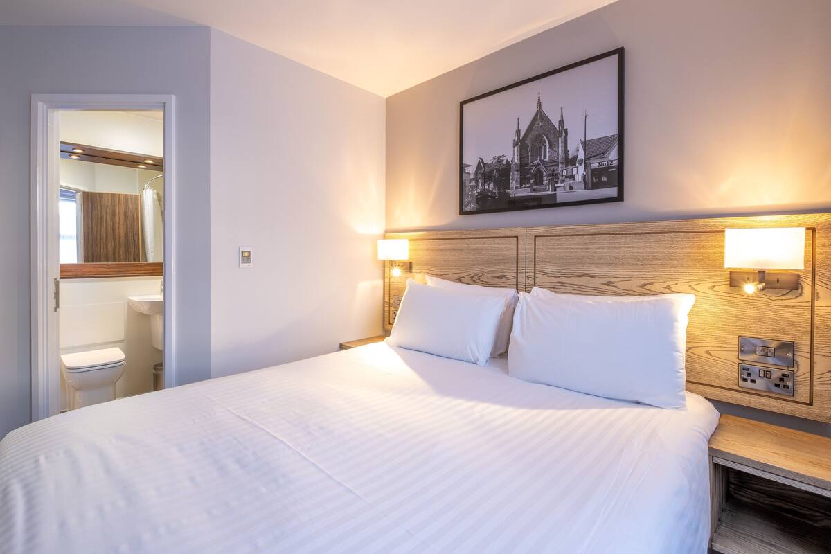 A neatly made bed with white linens, a wooden headboard, and two bedside lamps.
