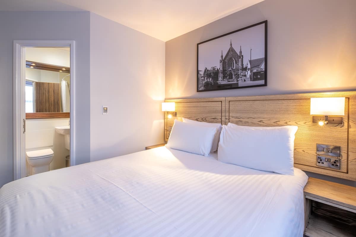 A neatly made bed with white linens, a wooden headboard, and two wall-mounted reading lamps.