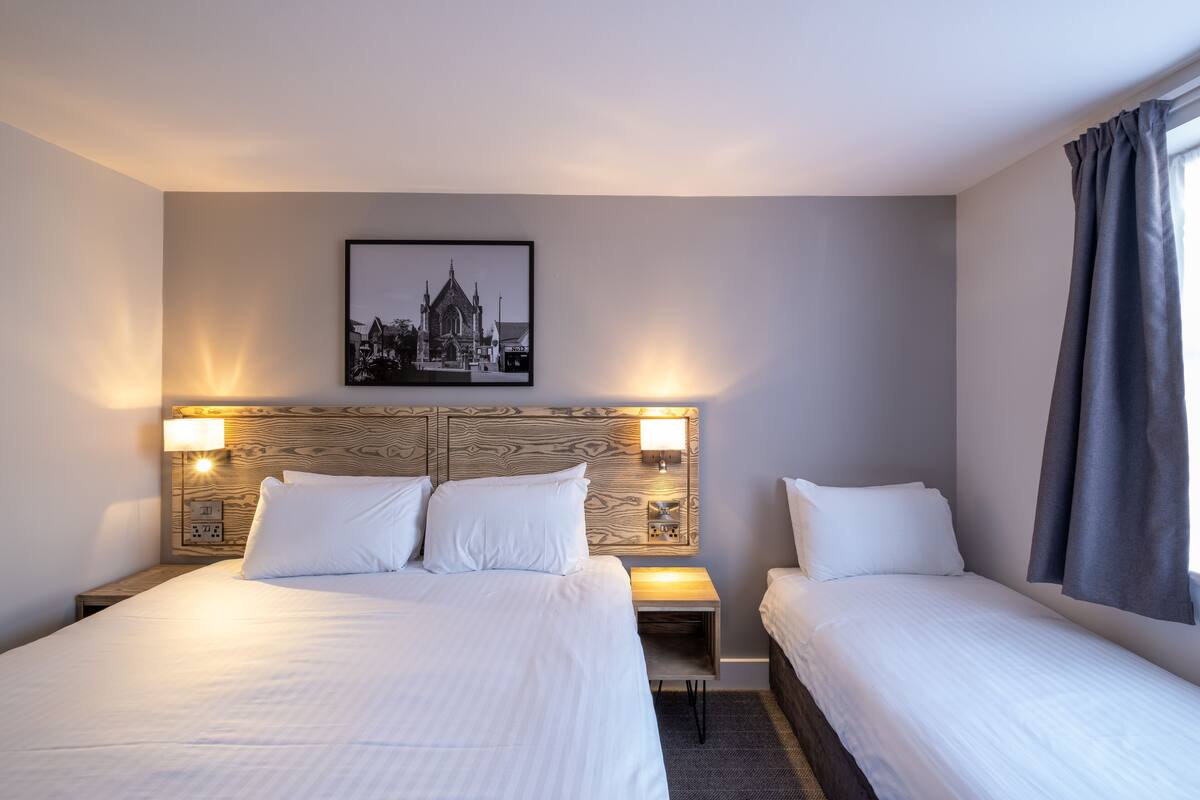 A hotel room with a large bed, two bedside tables, a nightstand, a wall-mounted picture, and a window with curtains.