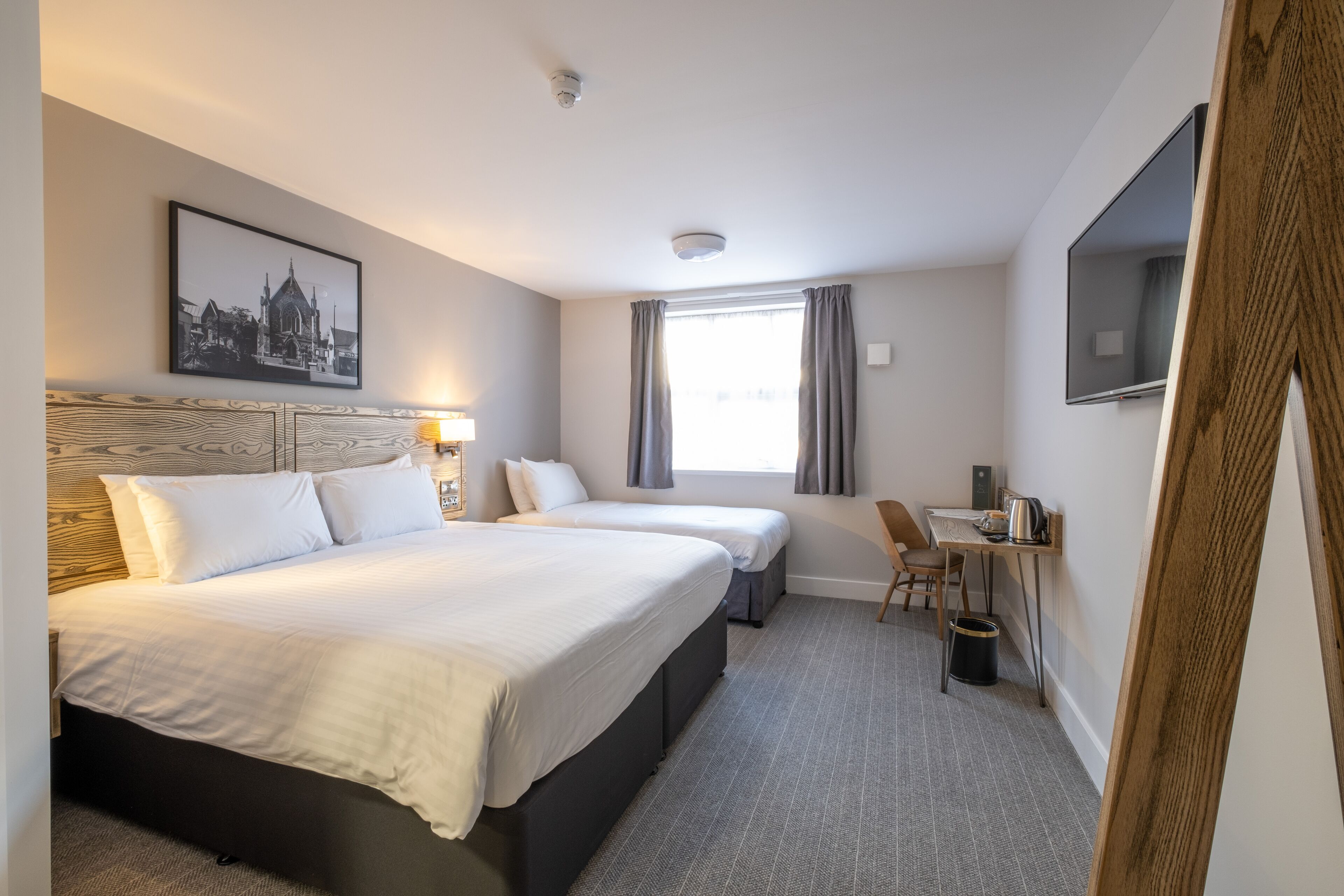 A hotel room with two beds, a desk, a chair, a TV, and a window with curtains.