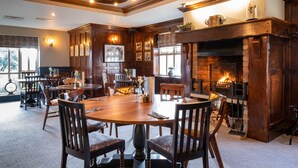 A spacious dining area with a large wooden table and chairs, a fireplace, and a chandelier. - Two Rivers, Chepstow by Marston’s Inns (Chepstow)