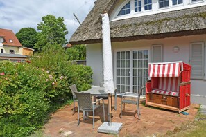 A patio with a table and chairs, a thatched-roof building, and a red and white striped bench.