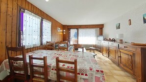 Une pièce chaleureuse avec un décor intérieur en bois, une table à manger avec des chaises, un coin cuisine et une grande fenêtre avec des rideaux.