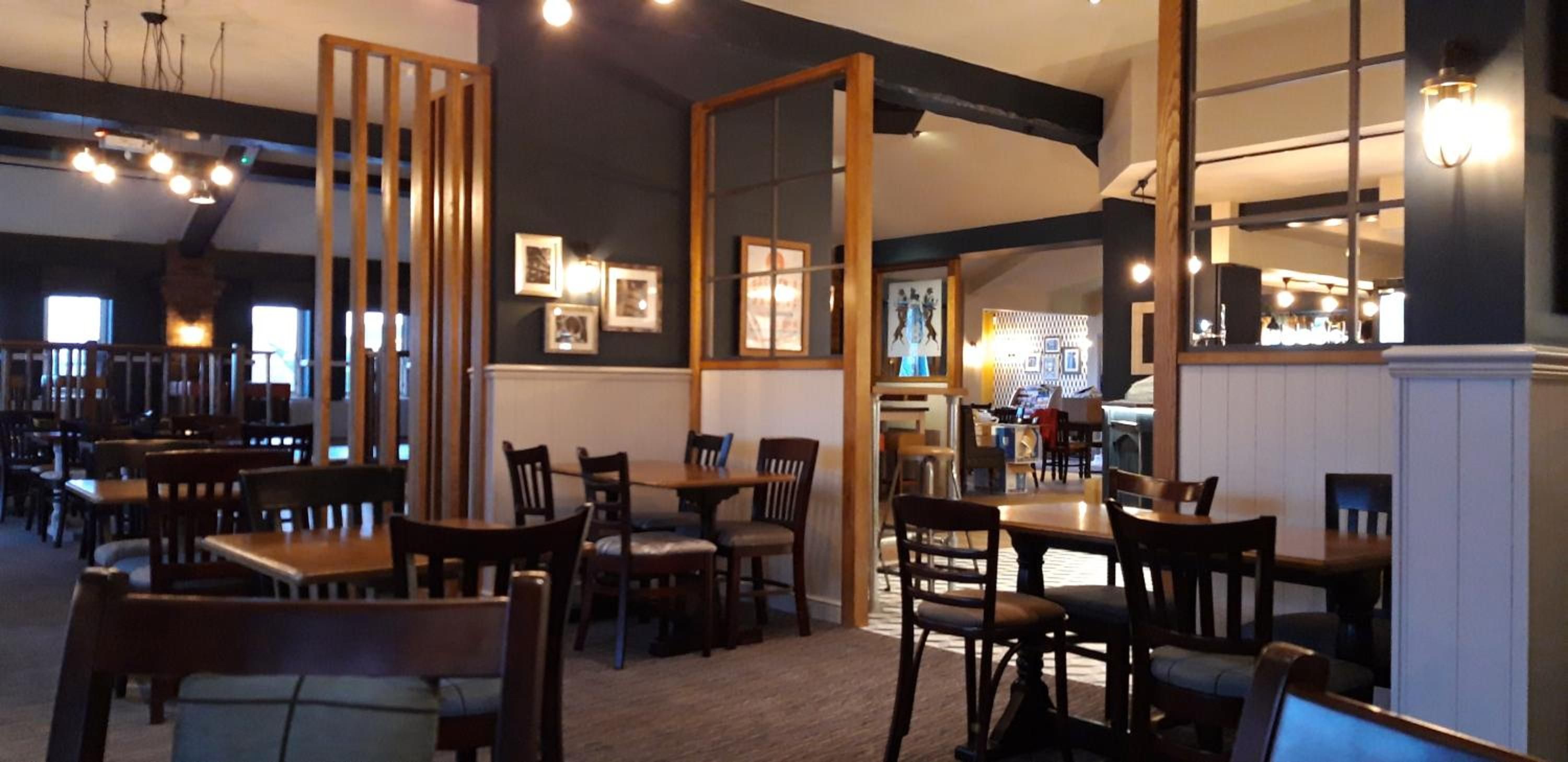Interior de un restaurante con mesas y sillas de madera, cuadros en las paredes y una zona de bar.
