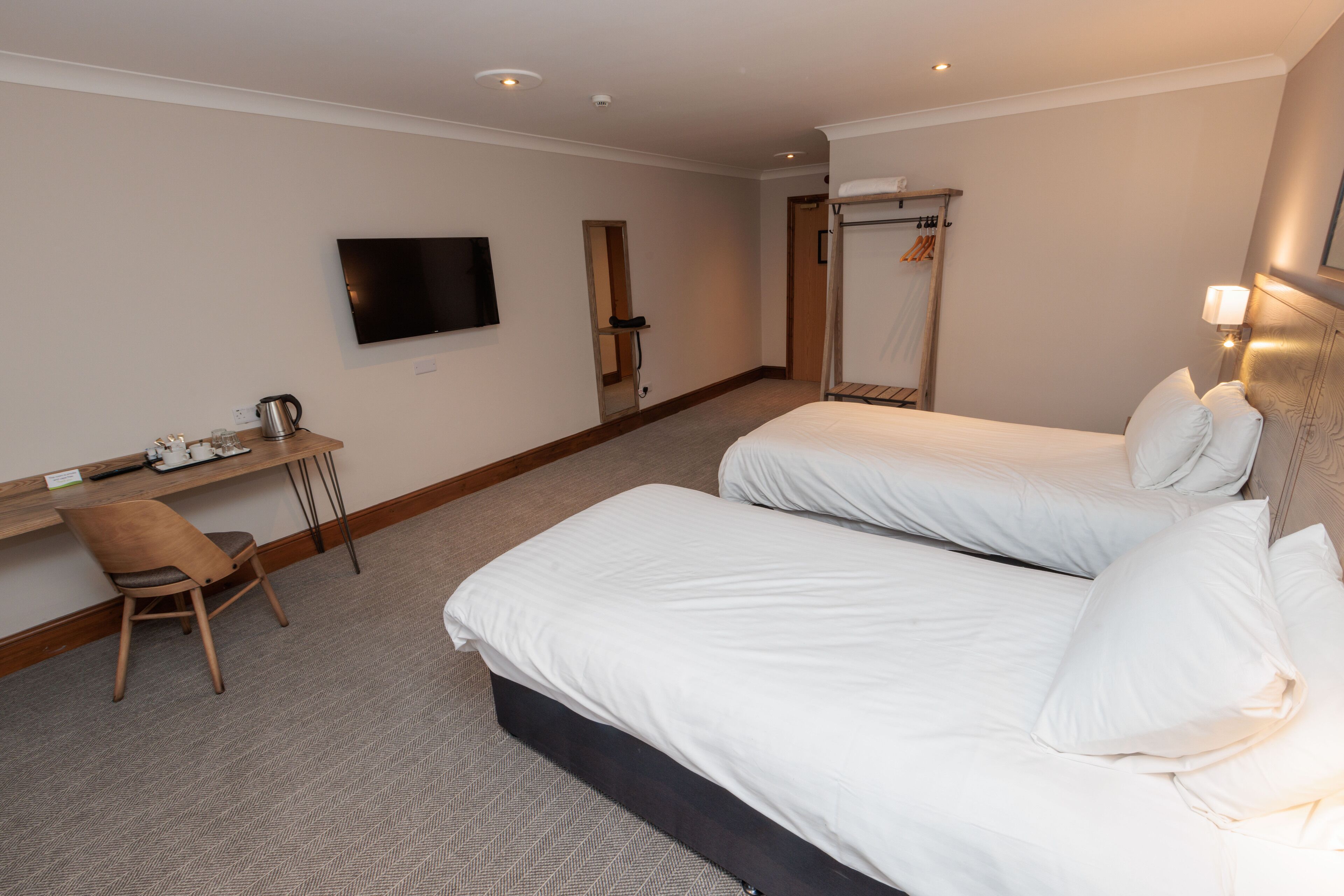 A hotel room with two beds, a desk with a chair, a television, and a mirror.