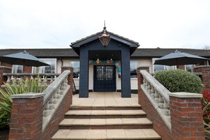 Un edificio de dos pisos con fachada azul oscuro, una puerta principal negra y un pequeño porche con escalones de acceso.