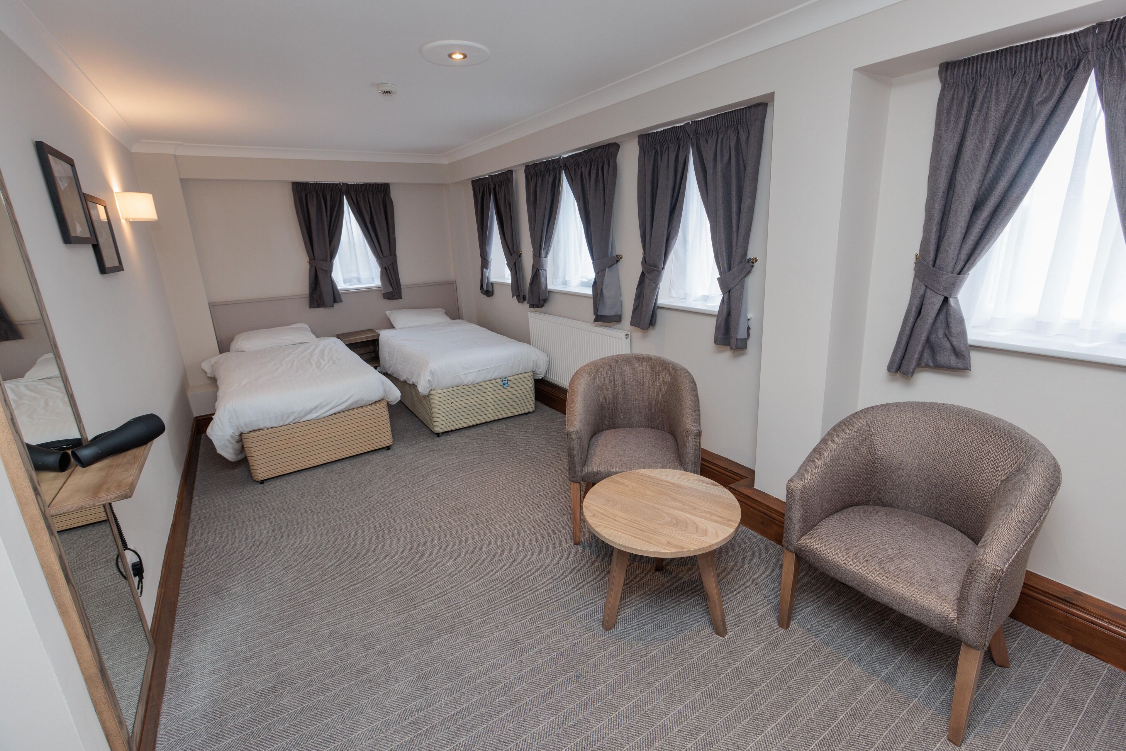 Habitación de hotel con dos camas, una silla, una mesita y un espejo.