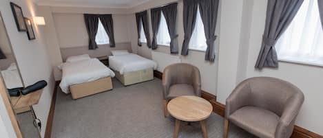 Habitación de hotel con dos camas, una silla, una mesita y un espejo.