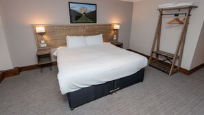 A neatly arranged hotel room with a large bed, bedside tables, a wooden headboard, a wall-mounted picture, and a clothing rack. - Boundary, Alfreton by Marston's Inns (Alfreton)