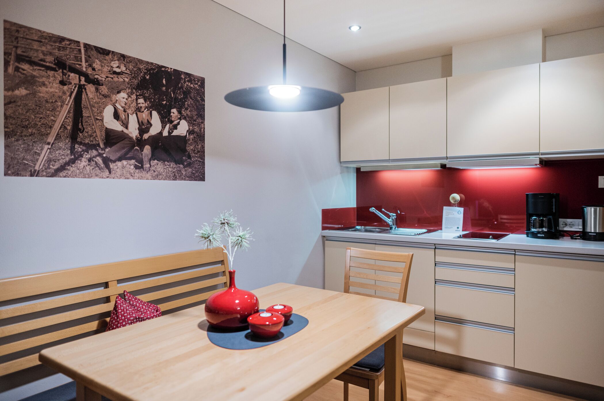 Een moderne keuken met een eethoek, een rode vaas met bloemen en een foto uit vervlogen tijden aan de muur.
