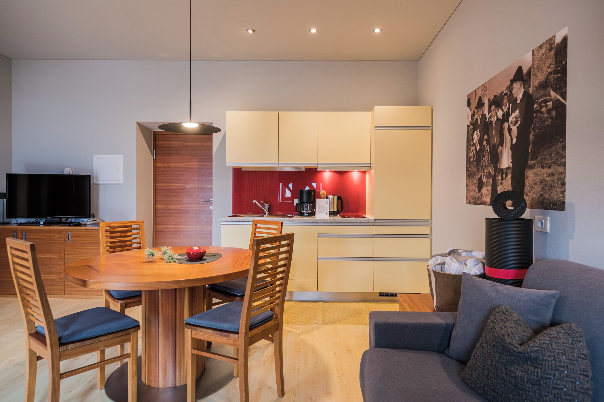 Een moderne woonkamer met een eethoek, een keuken met rode accenten, een flatscreen televisie en een groot poster aan de muur.
