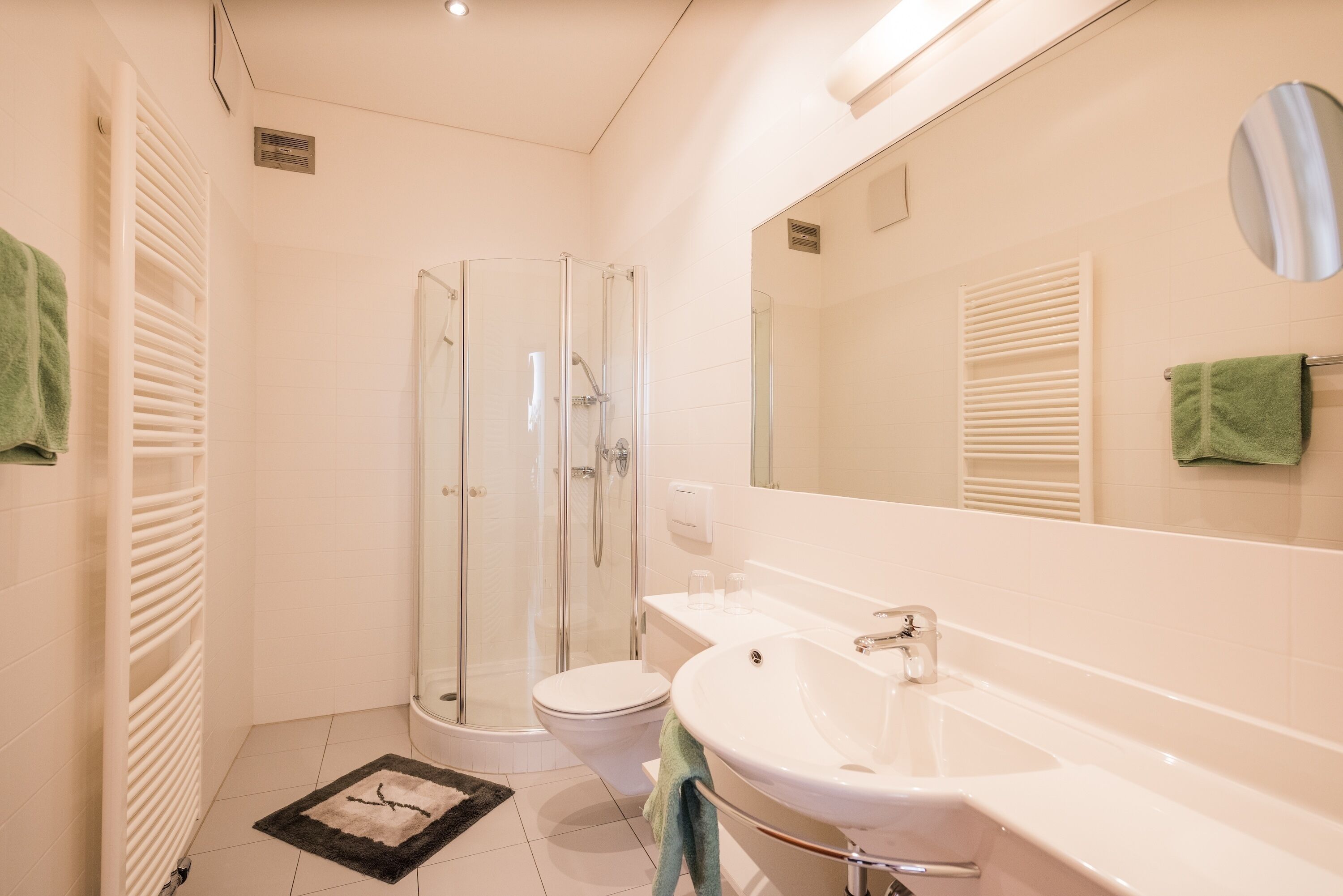 Een moderne badkamer met een glazen douchecabine, een wit wastafelmeubel en een toilet.