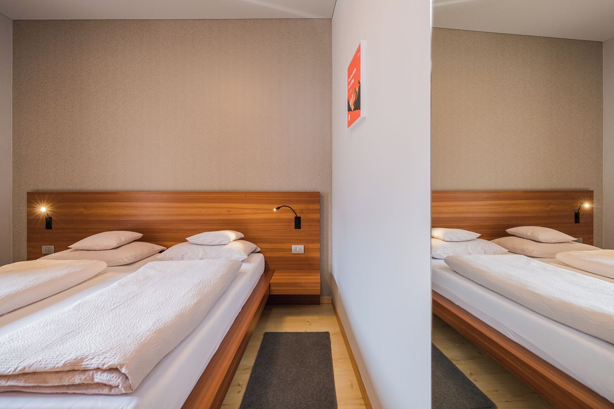 Ein Hotelzimmer mit zwei Einzelbetten, Holz-Kopfteilen und einer kleinen Wandleuchte.