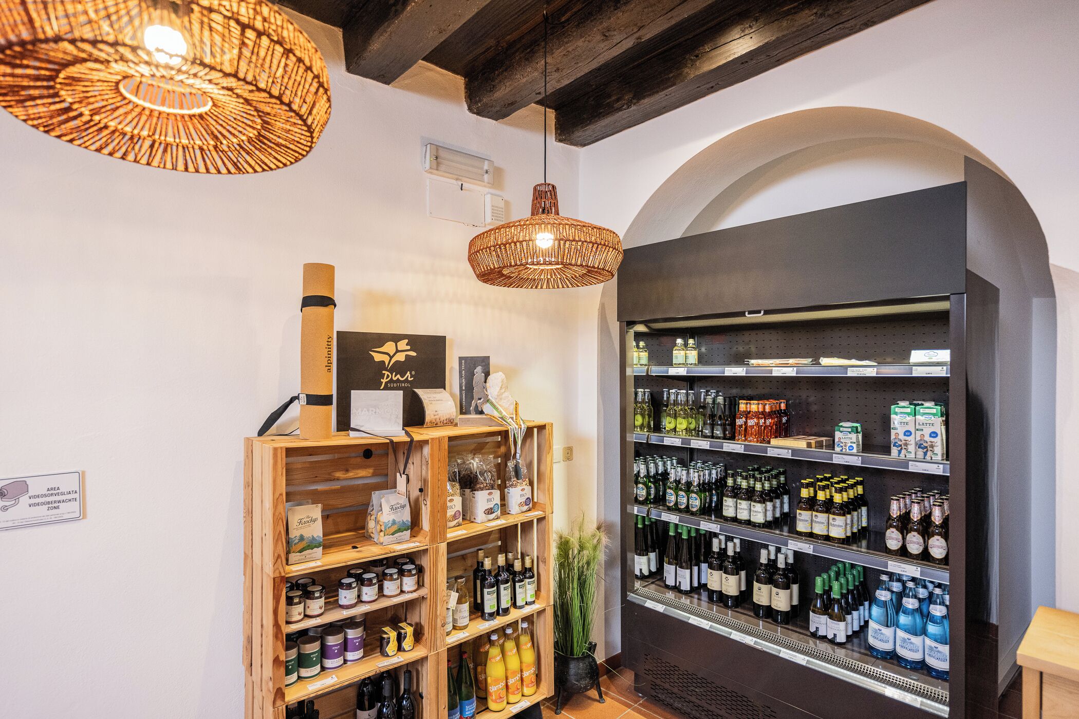 Una tienda con estantes llenos de diversas bebidas, una lámpara colgante de mimbre y un expositor de madera con botellas.