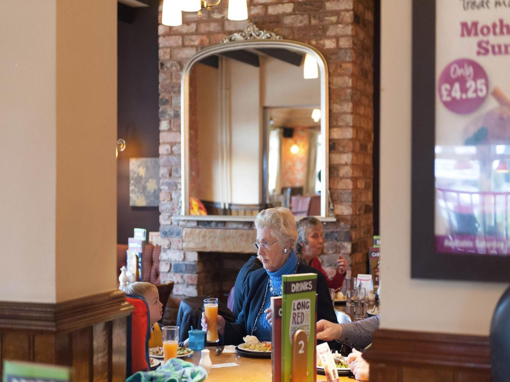 A restaurant interior with brick walls, a mirror, and a menu stand.