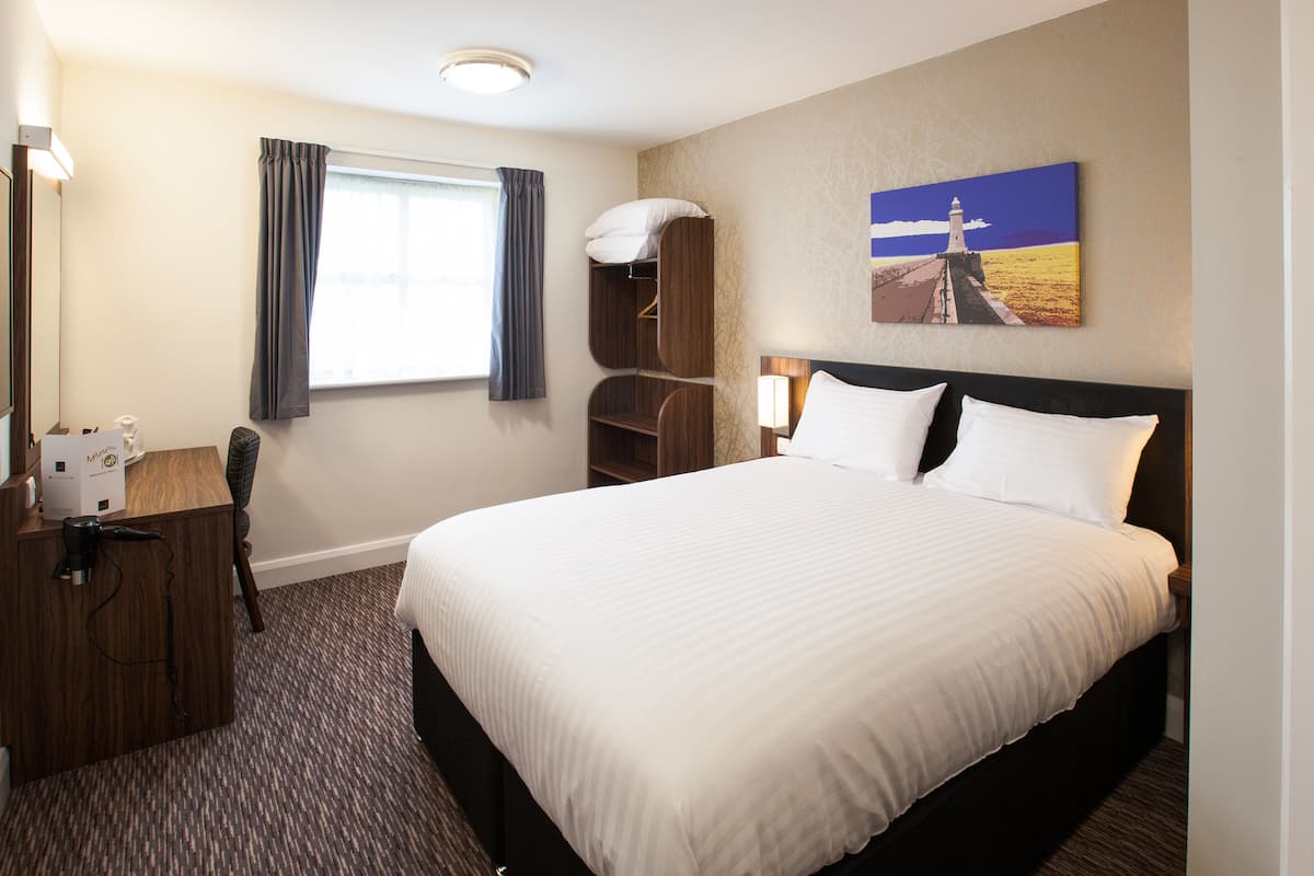 A hotel room with a large bed, a desk with a telephone, a mirror, and a window with curtains.