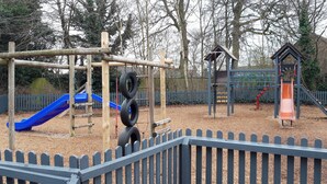 Ein Spielplatz mit einer blauen Rutsche, einer Reifenwand zum Klettern und einer kleinen Holzkonstruktion.