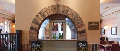 Mostrador de restaurante con un arco de ladrillo, un reloj encima y letreros que dicen 'Salsa de Verduras' y 'Salsa de Carne' a cada lado.