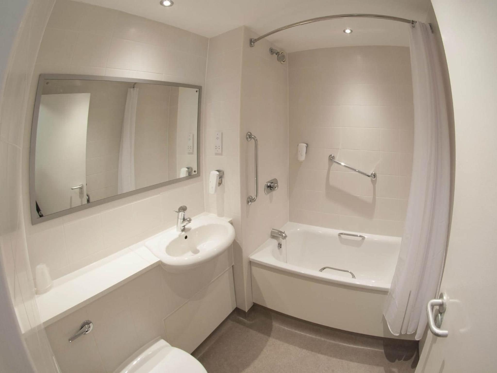 A modern bathroom with a sink, mirror, and bathtub.