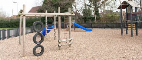 Un parque infantil con una estructura de neumáticos para escalar, un tobogán y una casita de madera.