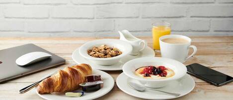 A breakfast setting with croissants, cereal, coffee, and juice on a wooden table.