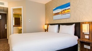 Ein Hotelzimmer mit einem großen Bett, zwei Nachttischlampen, einem Bild an der Wand und einer Tür zu einem Badezimmer.