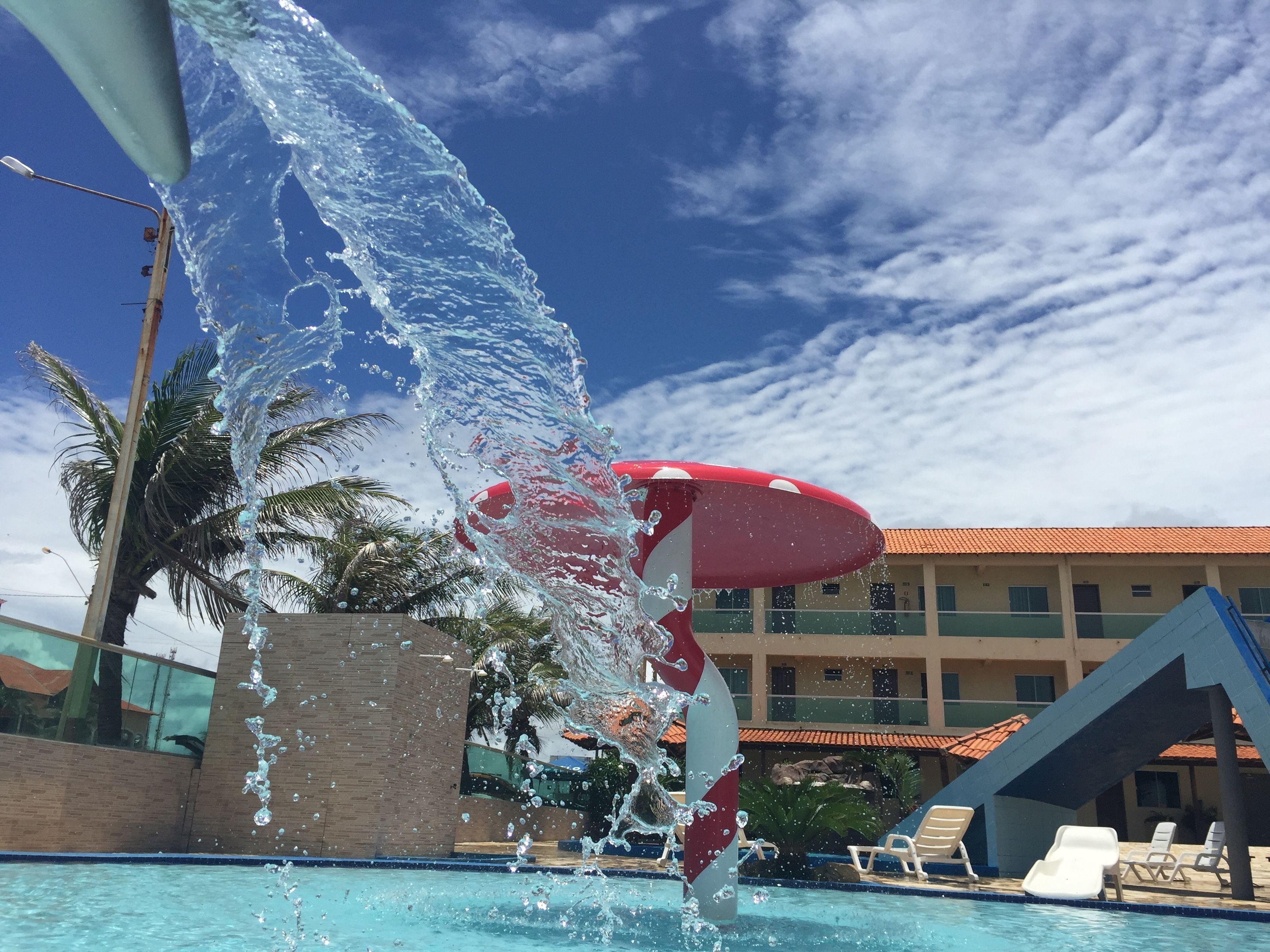 Una piscina con fuente, palmeras y un edificio con techo rojo al fondo.