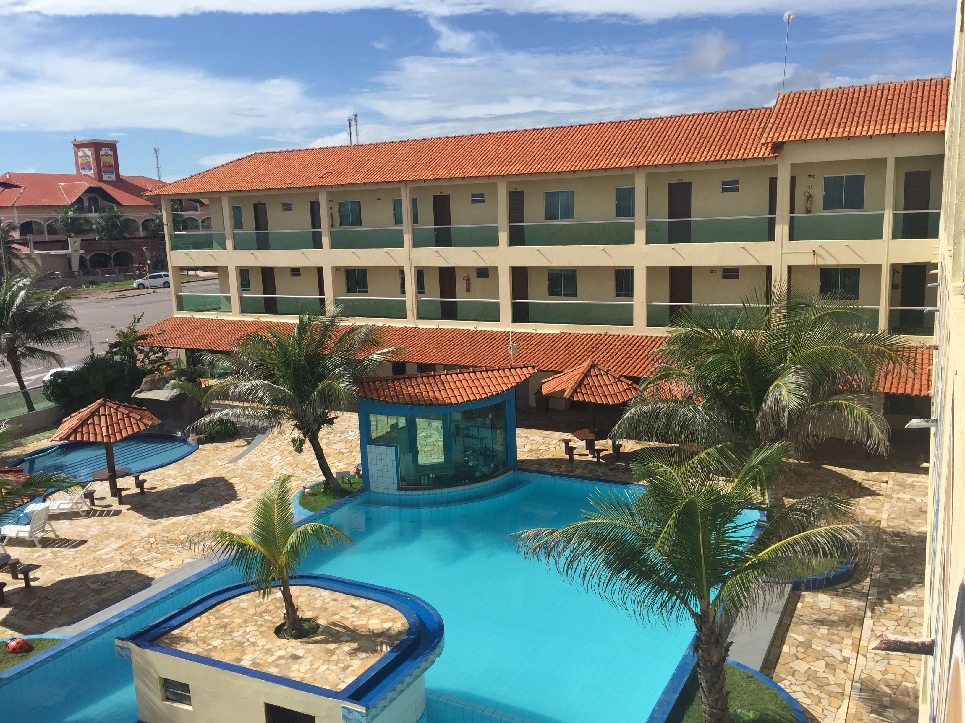 Un hôtel doté d’une piscine, de palmiers et d’un toit recouvert de tuiles rouges.