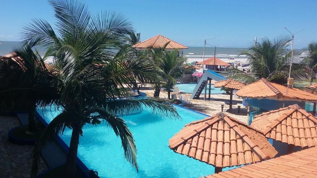 A pool area with palm trees, a slide, and a beach view.