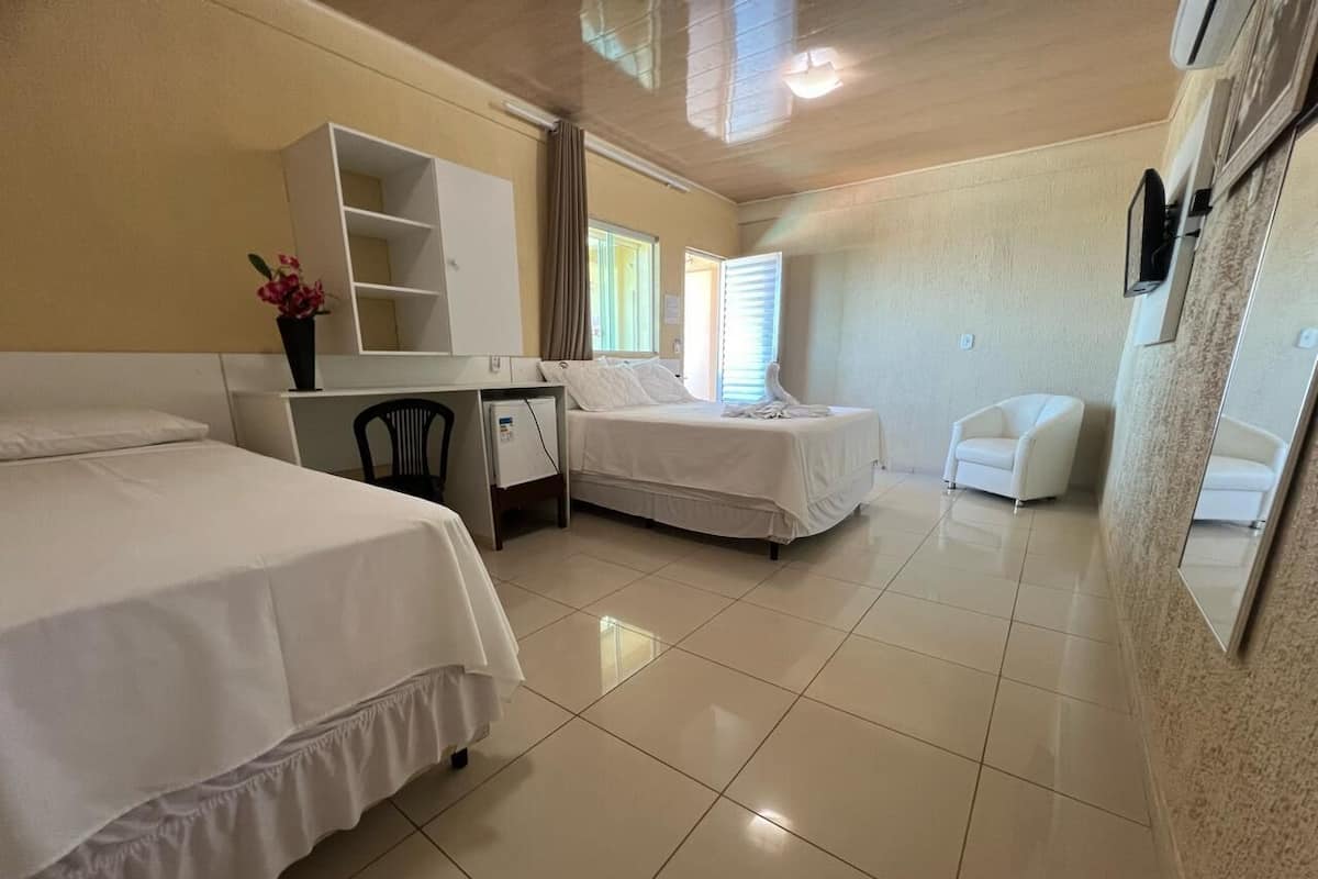Quarto de hotel com duas camas, uma escrivaninha, uma cadeira, uma televisão e um espelho.