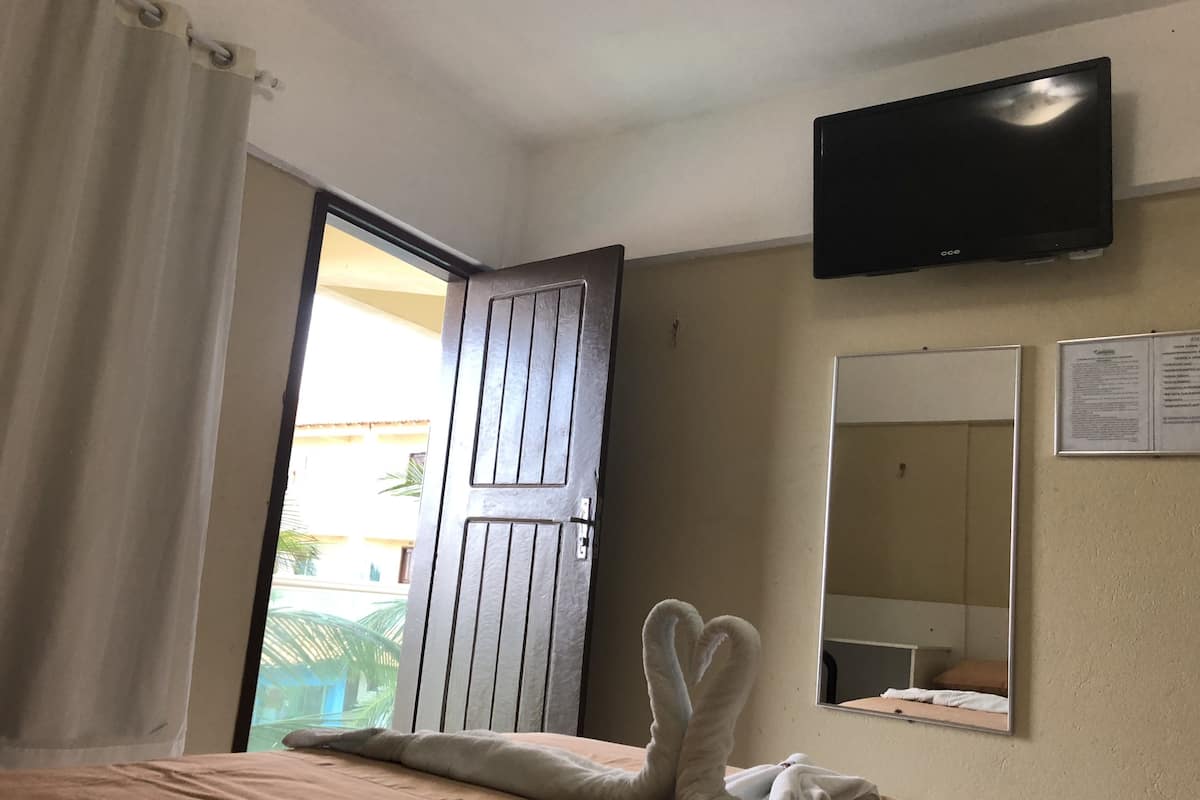 Quarto de hotel com uma cama, uma televisão presa à parede, uma porta e uma janela.