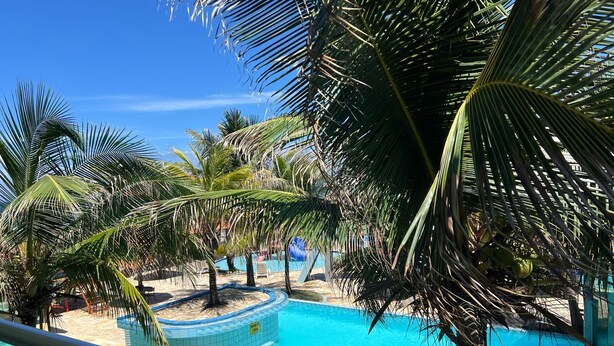 A pool area with palm trees and a clear blue sky. - Hotel Concha do Mar (Salinópolis)