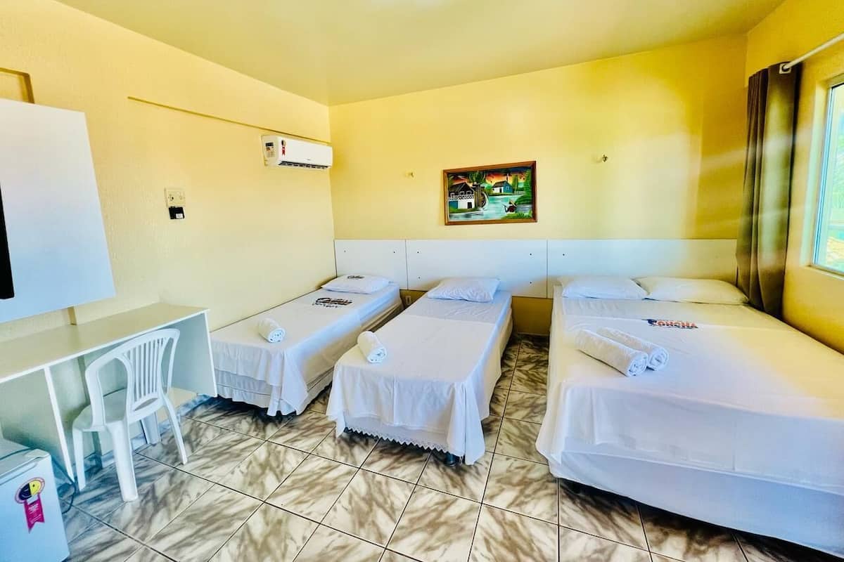 Quarto de hotel com três camas de solteiro, uma escrivaninha e uma cadeira.