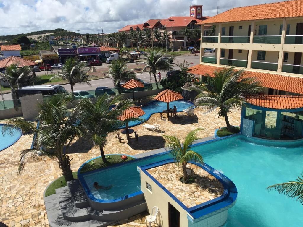 Een resort met meerdere zwembaden, palmbomen en een groot gebouw met een rood dak.