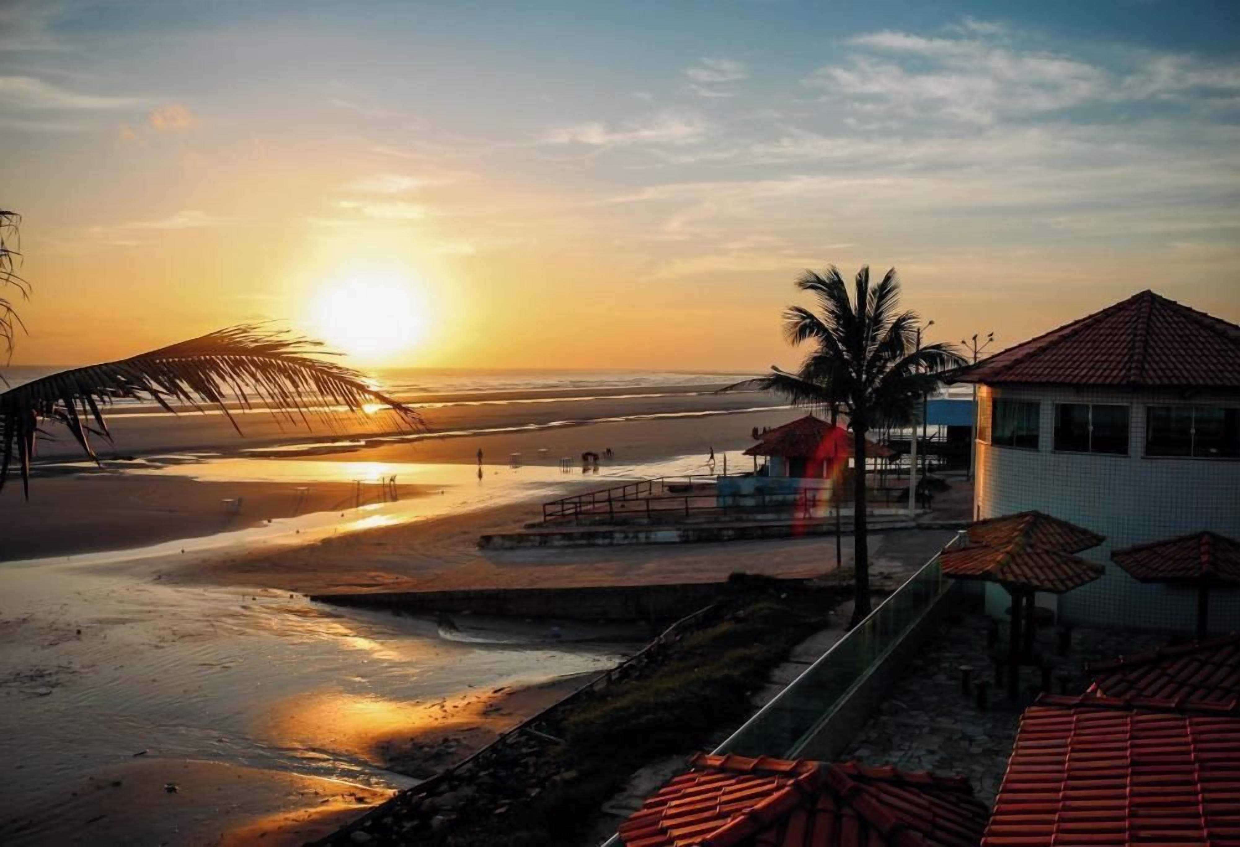 Una spiaggia con un tramonto, palme e un edificio con tetto rosso.